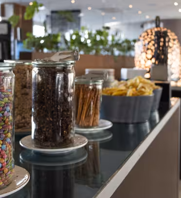 En buffet i en moderne restaurant med krukker med farverigt slik, korn, kringler og en bakke kartoffelchips arrangeret på en disk. Potteplanter og dekorative lamper er i baggrunden. Indstillingen er lyse og rene.